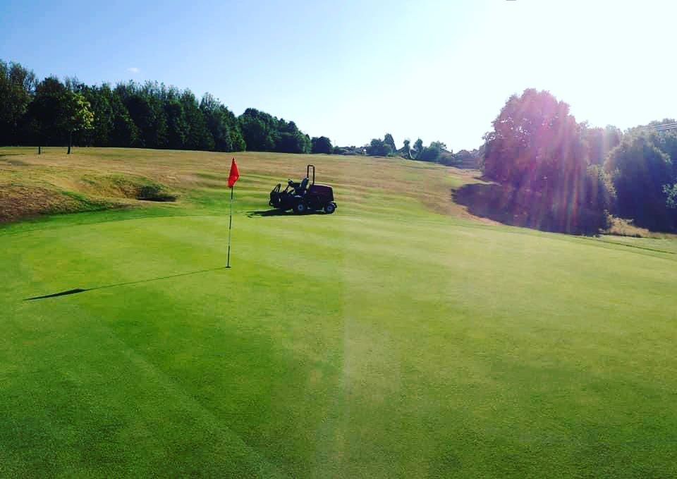 Greenkeeper mowing the course on a sunny day